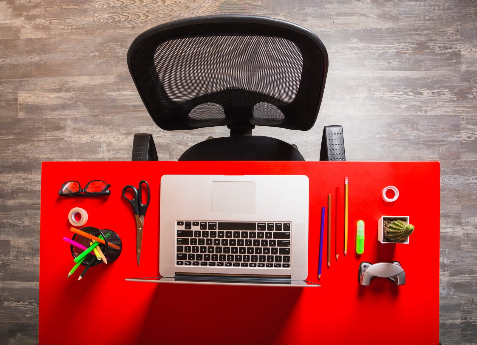 Red office desk with laptop and stationery, top-down view